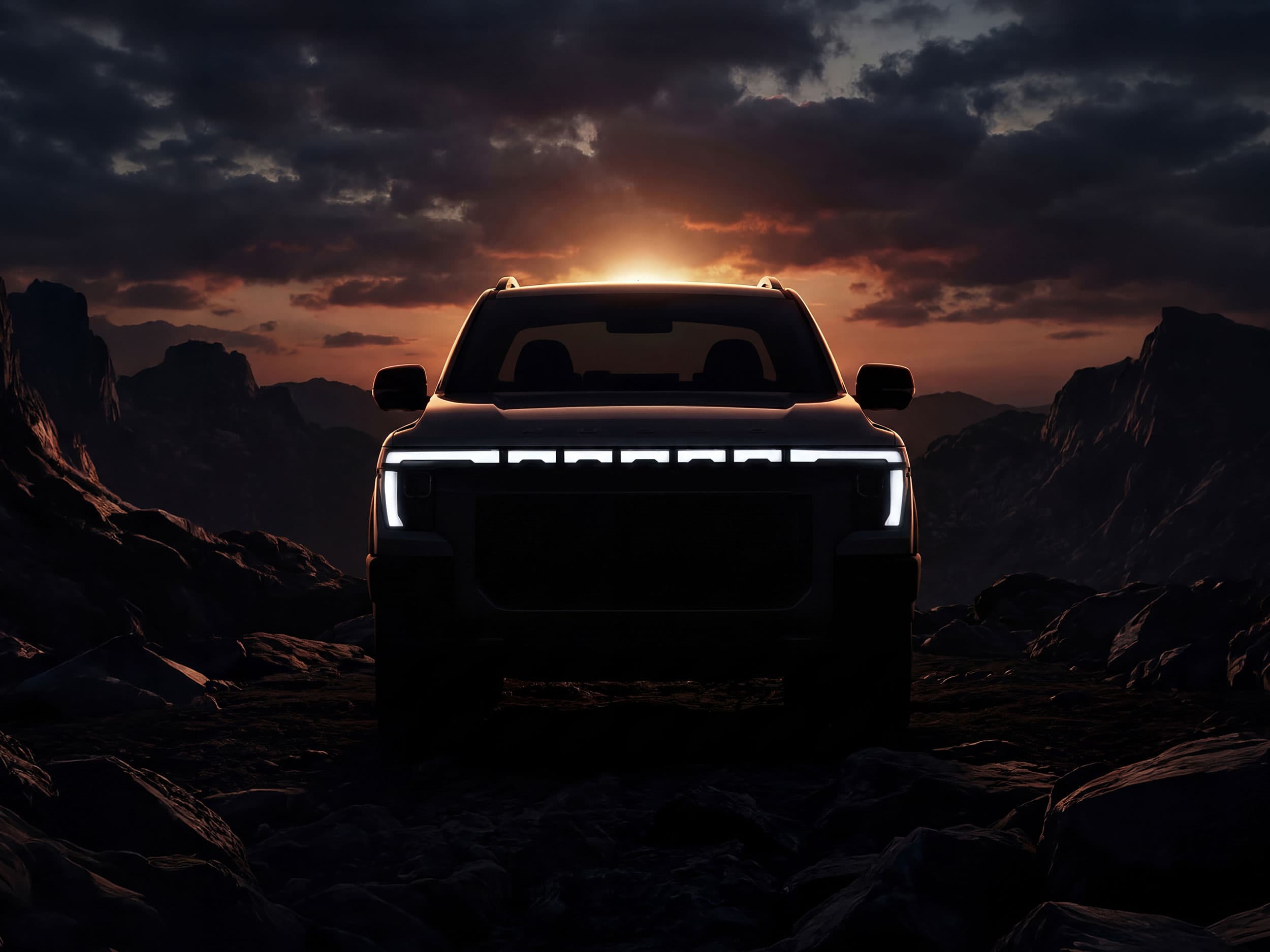 A Musso with illuminated headlights is silhouetted against a dramatic sunset backdrop in a mountainous landscape.