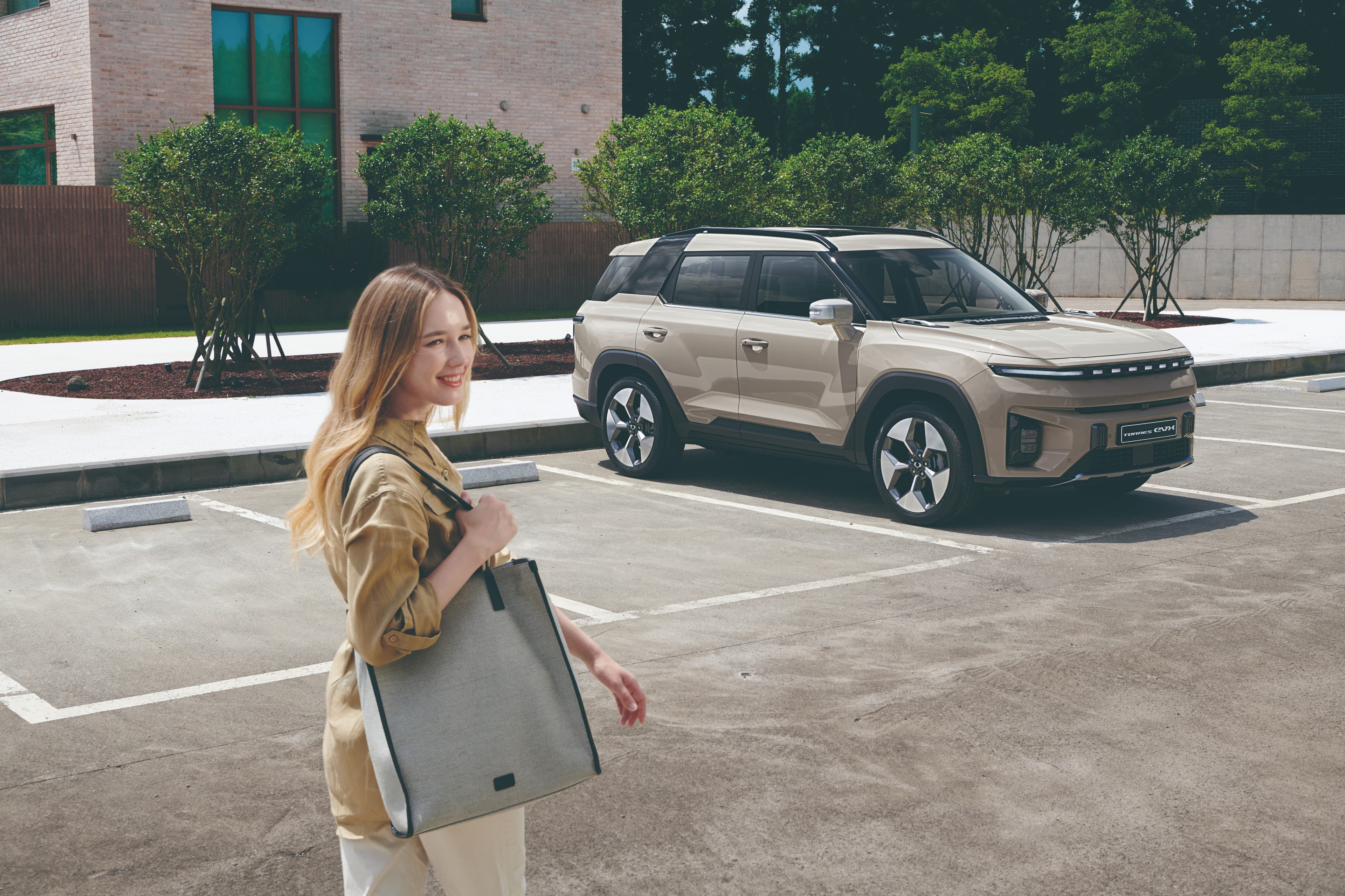 De Torres EVX in latté beige kleur die op een parking staat en een vrouw met grote handtas die ernaar toe stapt
