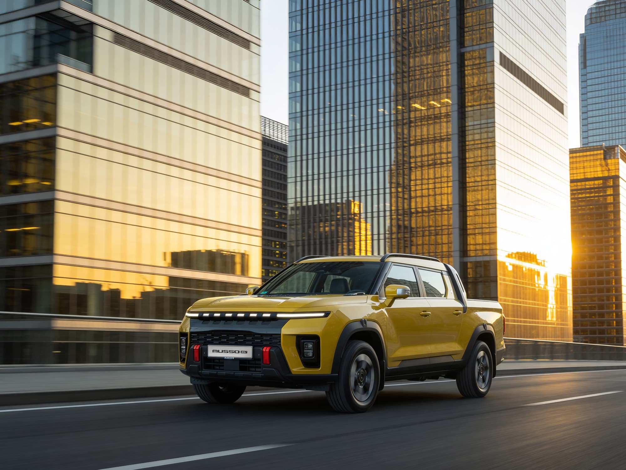 Yellow Musso EV driving through a city with tall, reflective buildings during sunset.