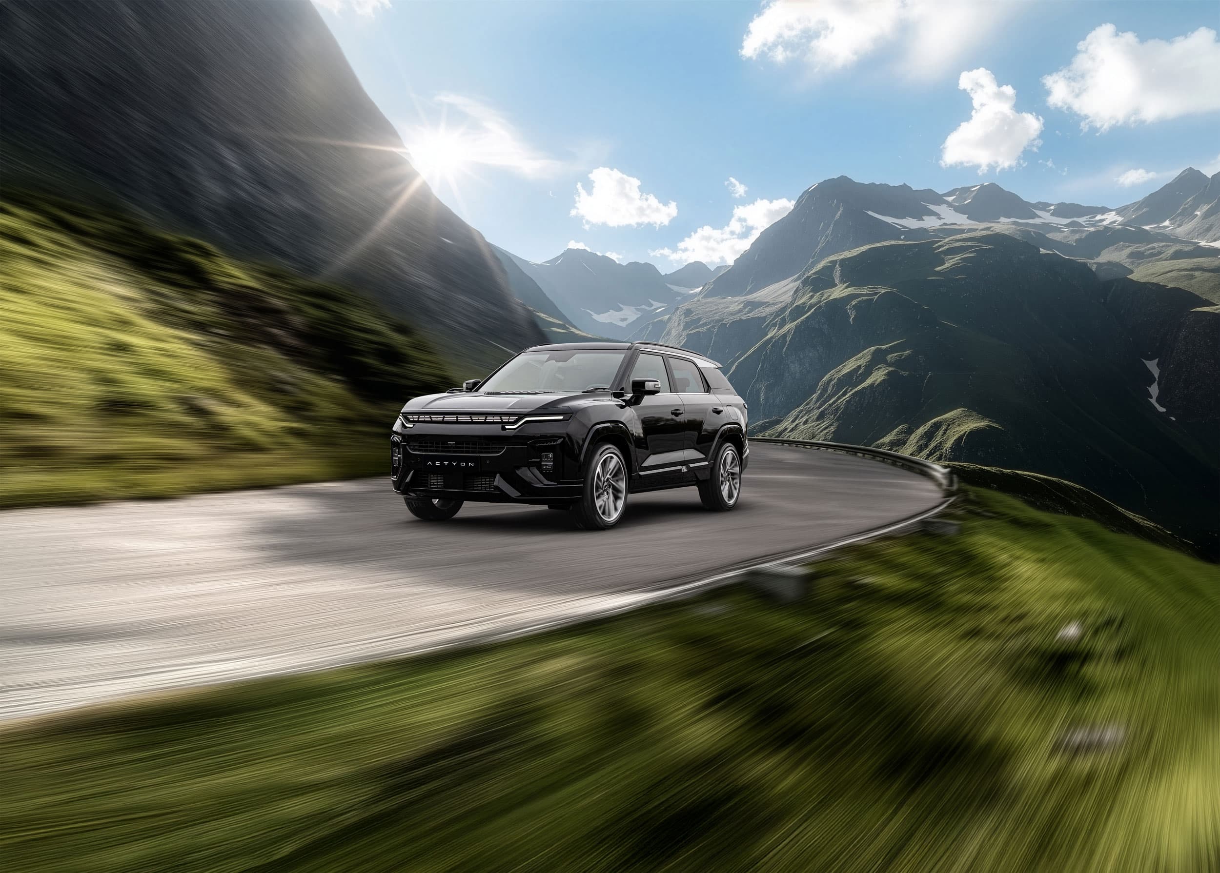 A black KGM Actyon driving on a winding mountain road with green hills and a bright sunlit sky in the background.